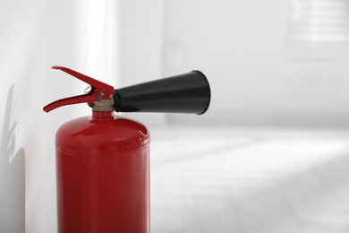 Photo of Fire extinguisher near white wall indoors, closeup. Space for text
