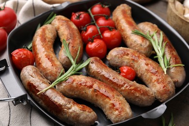 Photo of Grill pan with tasty homemade sausages, rosemary and tomatoes on table, closeup