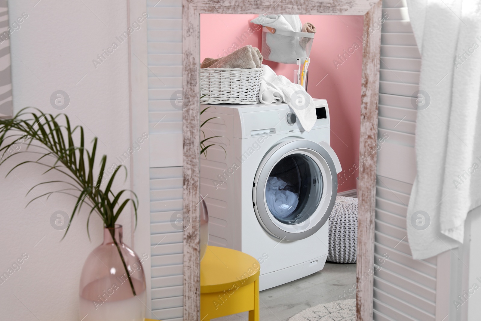 Photo of Reflection of modern washing machine in mirror at home. Laundry room