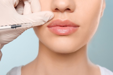 Photo of Young woman getting lip injection on color background, closeup