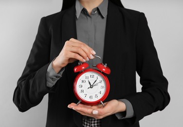 Photo of Businesswoman holding alarm clock on light grey  background, closeup. Time management