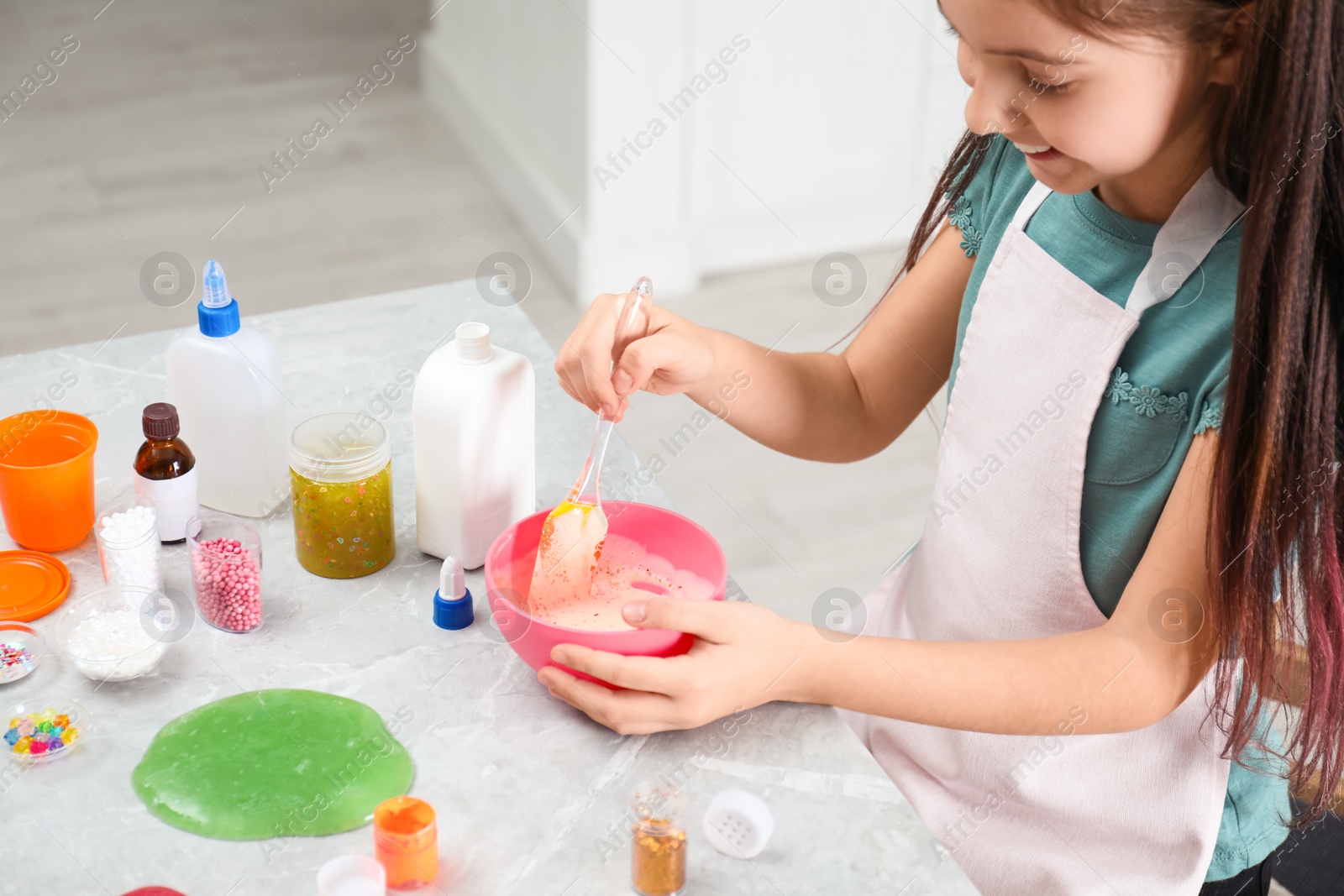 Photo of Little girl mixing ingredients with silicone spatula at table indoors, closeup. DIY slime toy