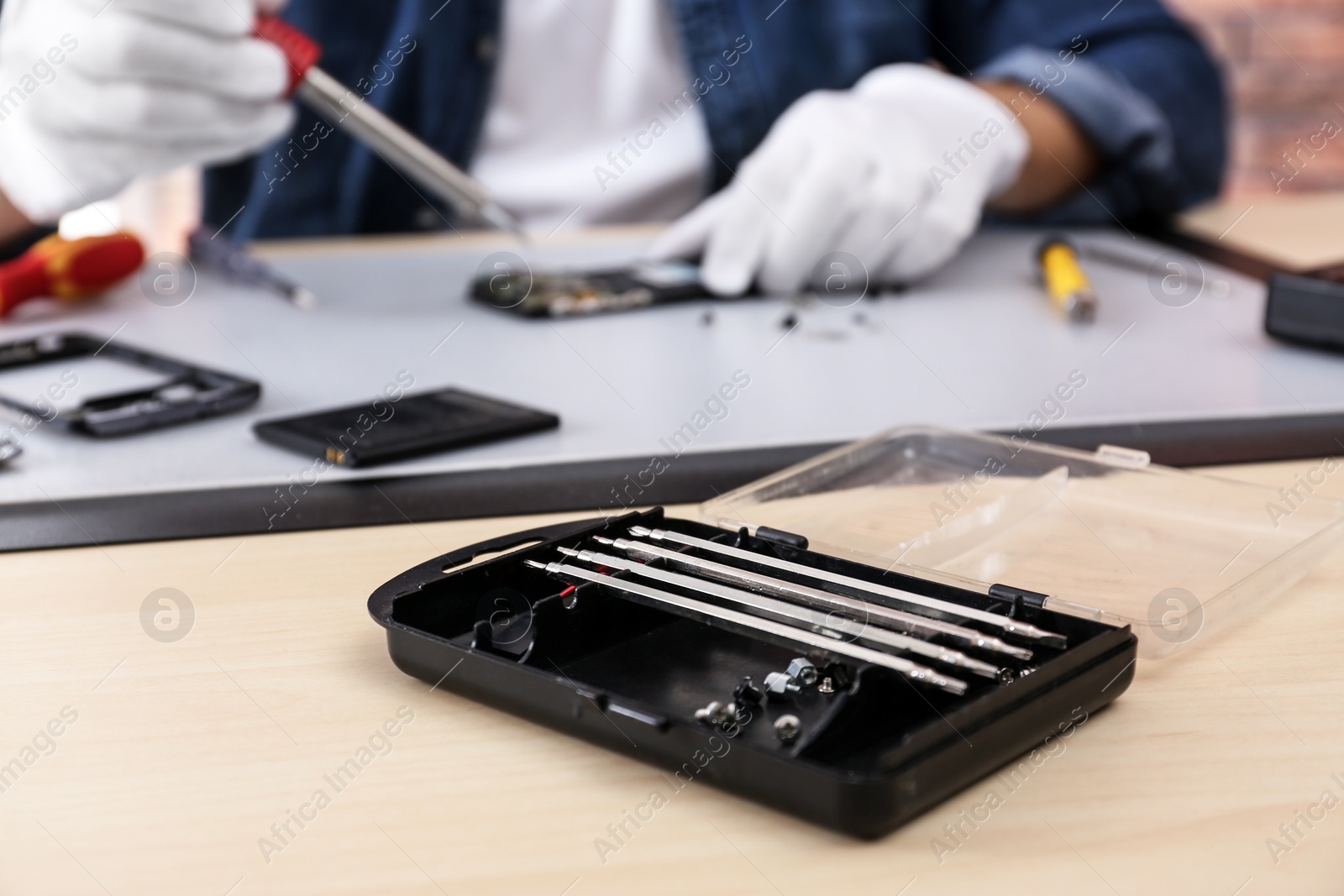 Photo of Technician repairing broken smartphone at table, focus on toolbox with screwdriver security bits. Space for text