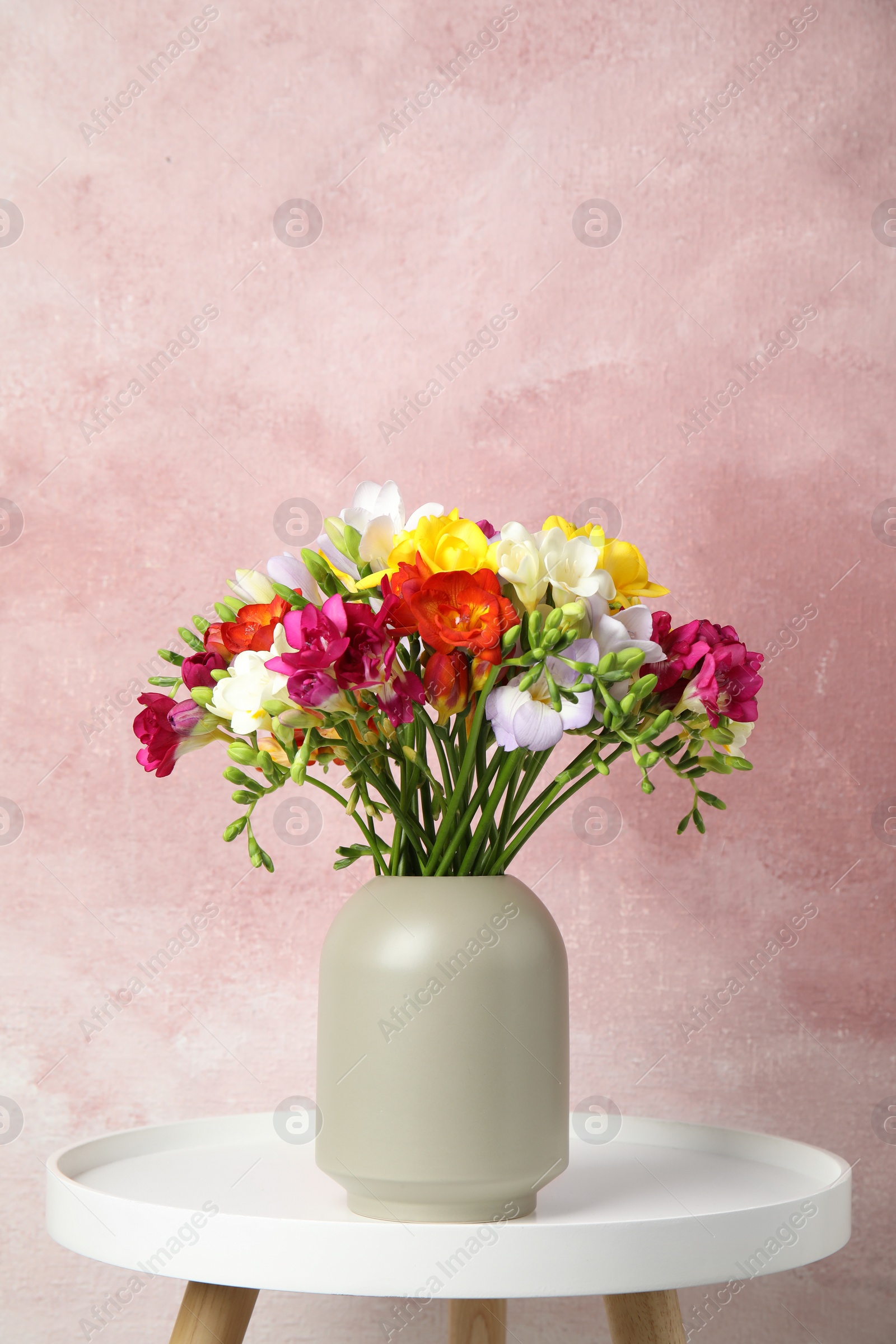 Photo of Bouquet of spring freesia flowers in vase on table against color background. Space for text