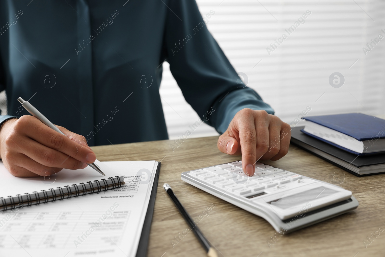 Photo of Woman using calculator while taking notes at wooden table, closeup