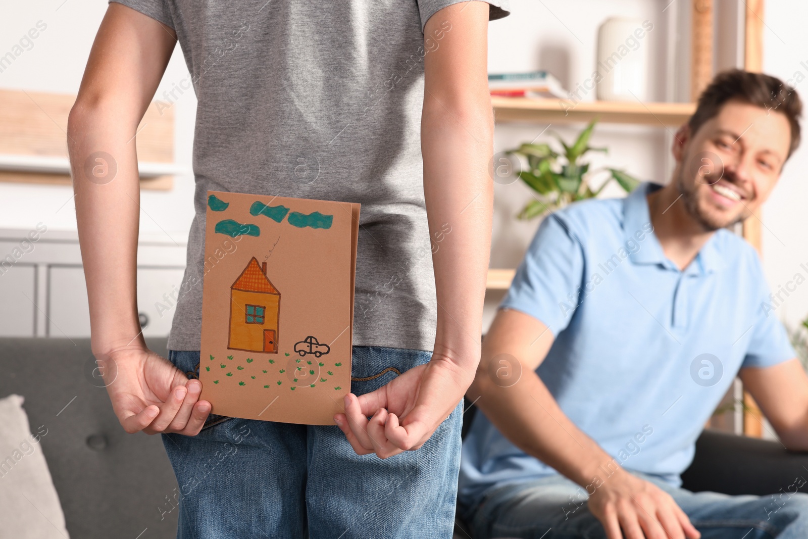 Photo of Boy hiding greeting card for his father behind back at home