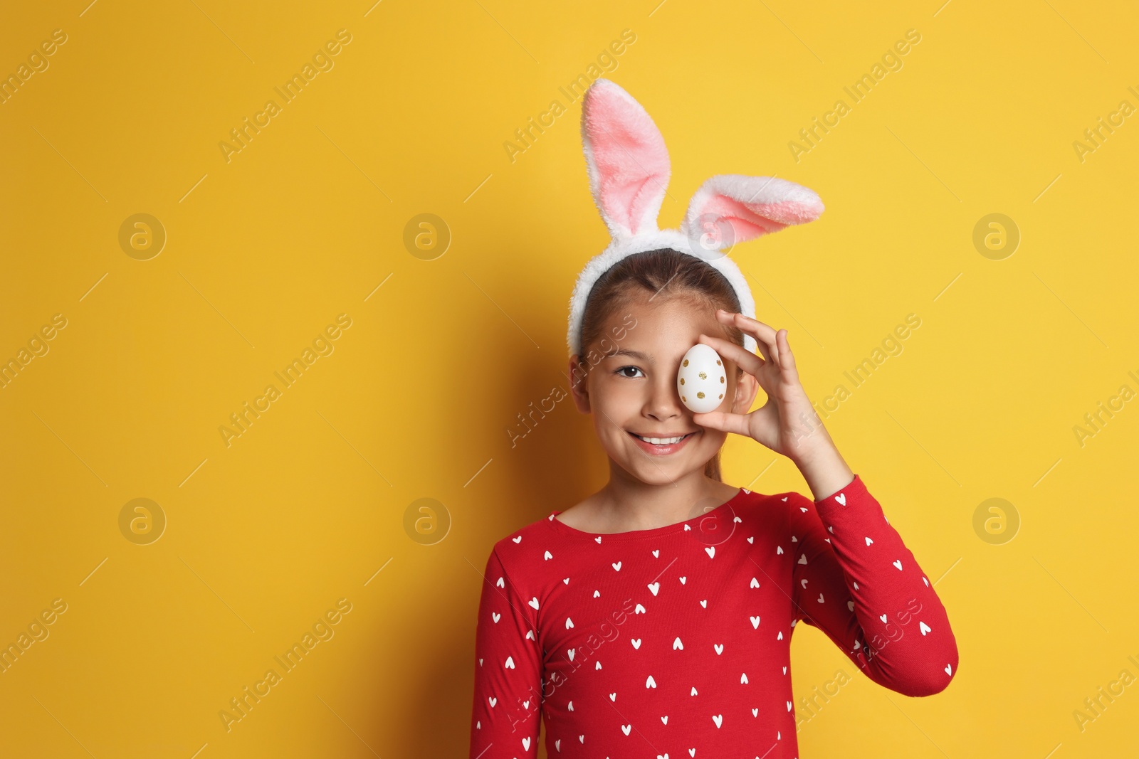 Photo of Cute happy girl with bunny ears and Easter egg against yellow background. Space for text