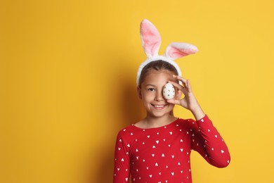 Cute happy girl with bunny ears and Easter egg against yellow background. Space for text