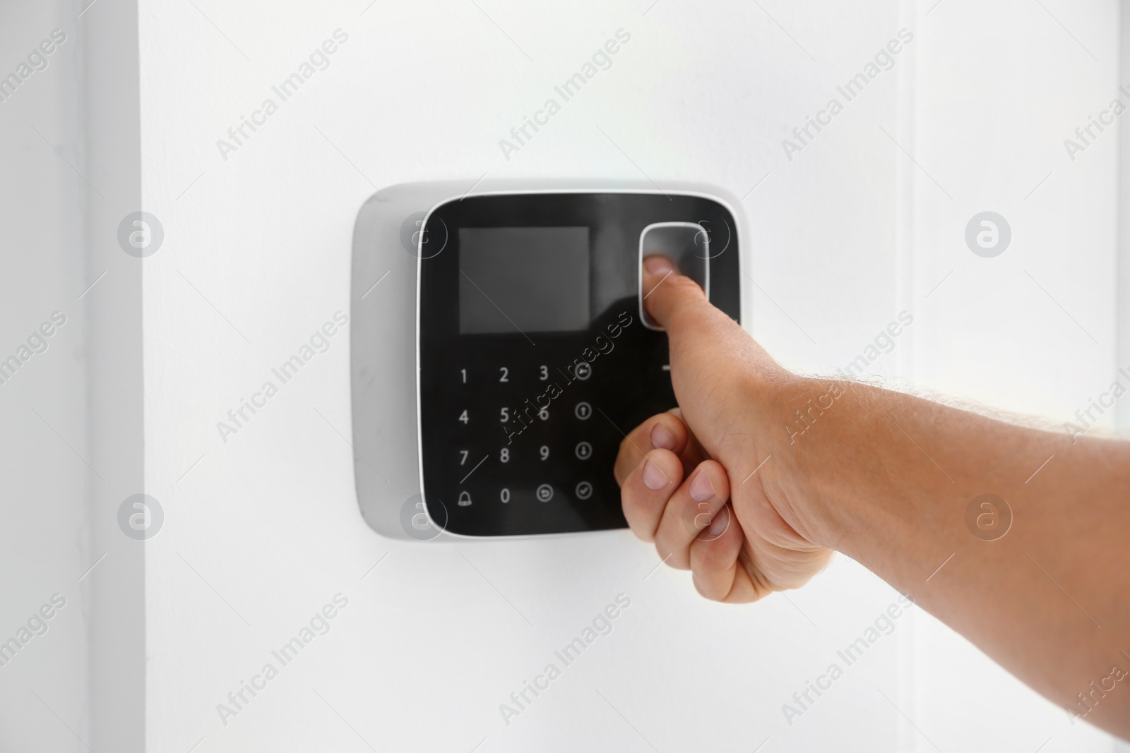 Photo of Mature man entering code on alarm system keypad indoors