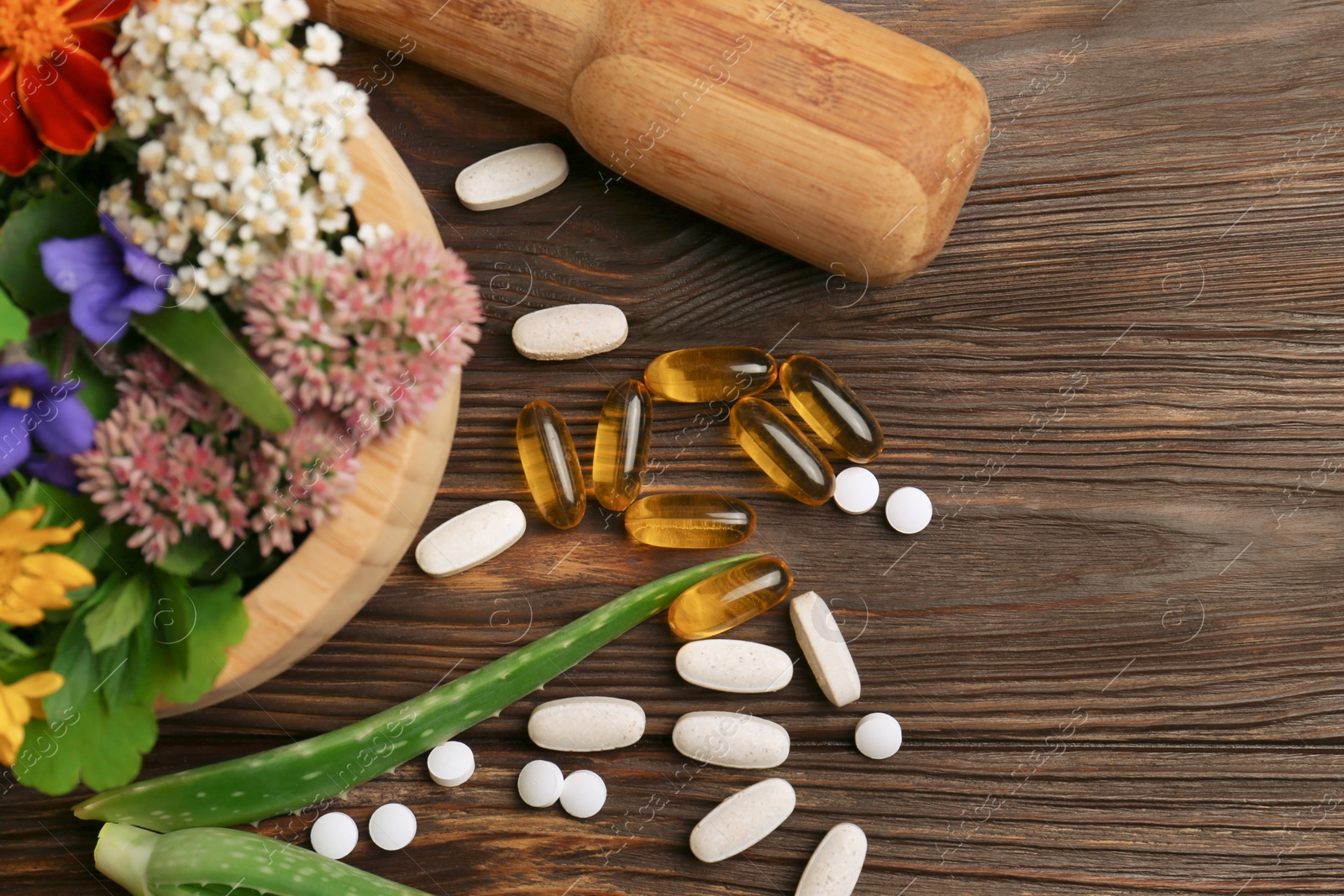 Photo of Mortar with fresh herbs, flowers and pills on wooden table, flat lay