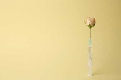 Photo of Medical syringe and rose flower on pale yellow background. Space for text