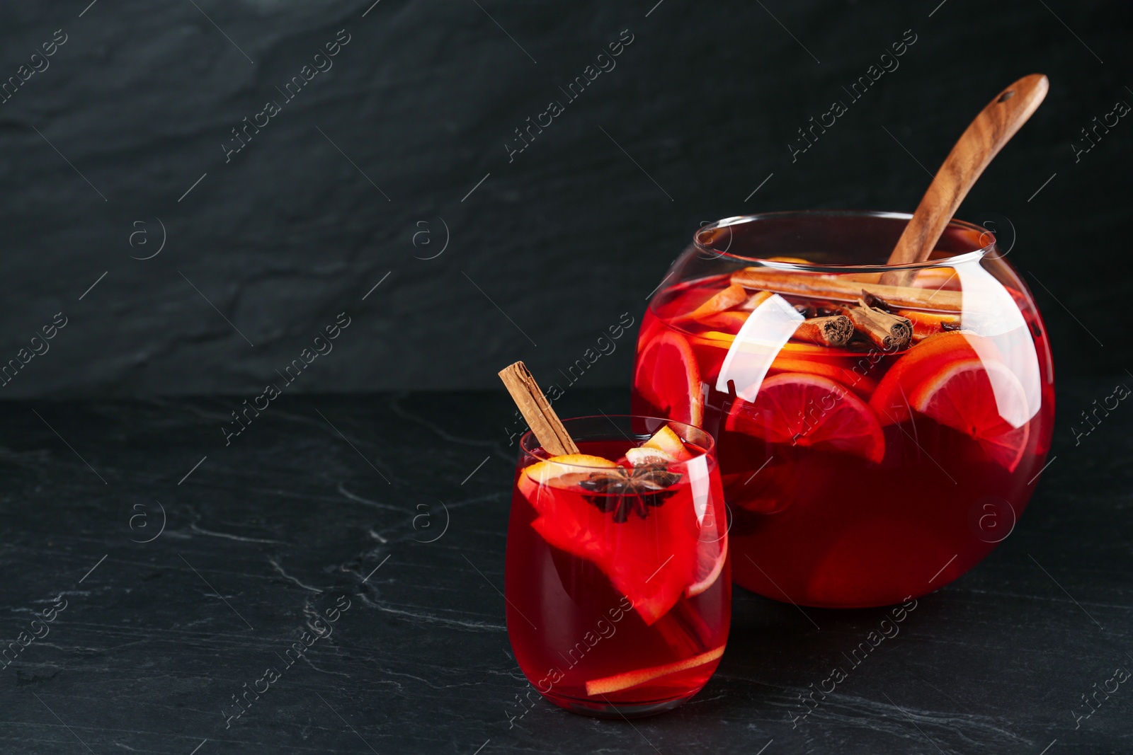 Photo of Glass and bowl of delicious aromatic punch drink on black table. Space for text