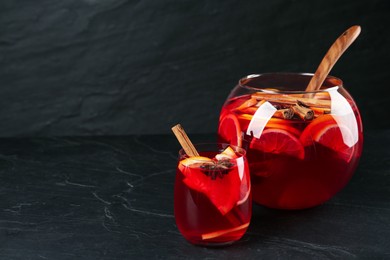 Photo of Glass and bowl of delicious aromatic punch drink on black table. Space for text