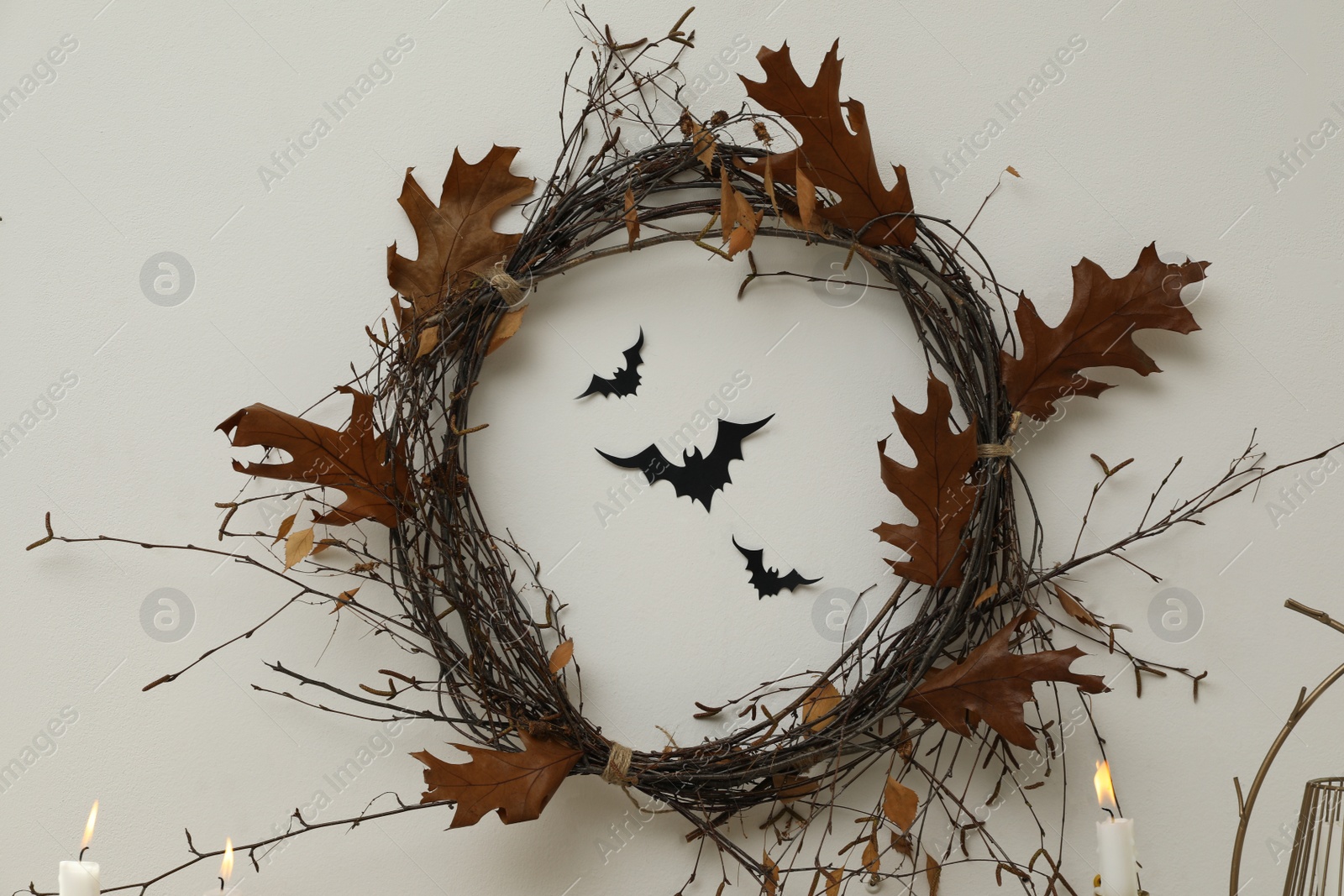 Photo of Wreath made with dry branches and leaves on white wall. Halloween decor