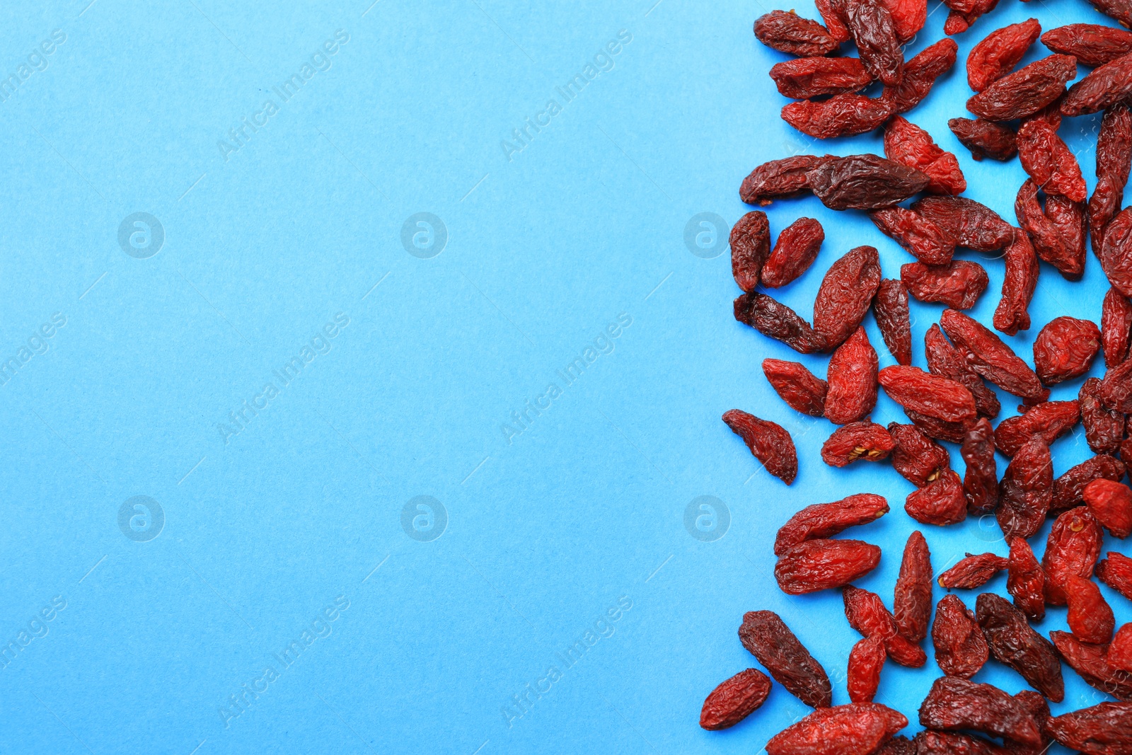 Photo of Dried goji berries on light blue background, flat lay. Space for text