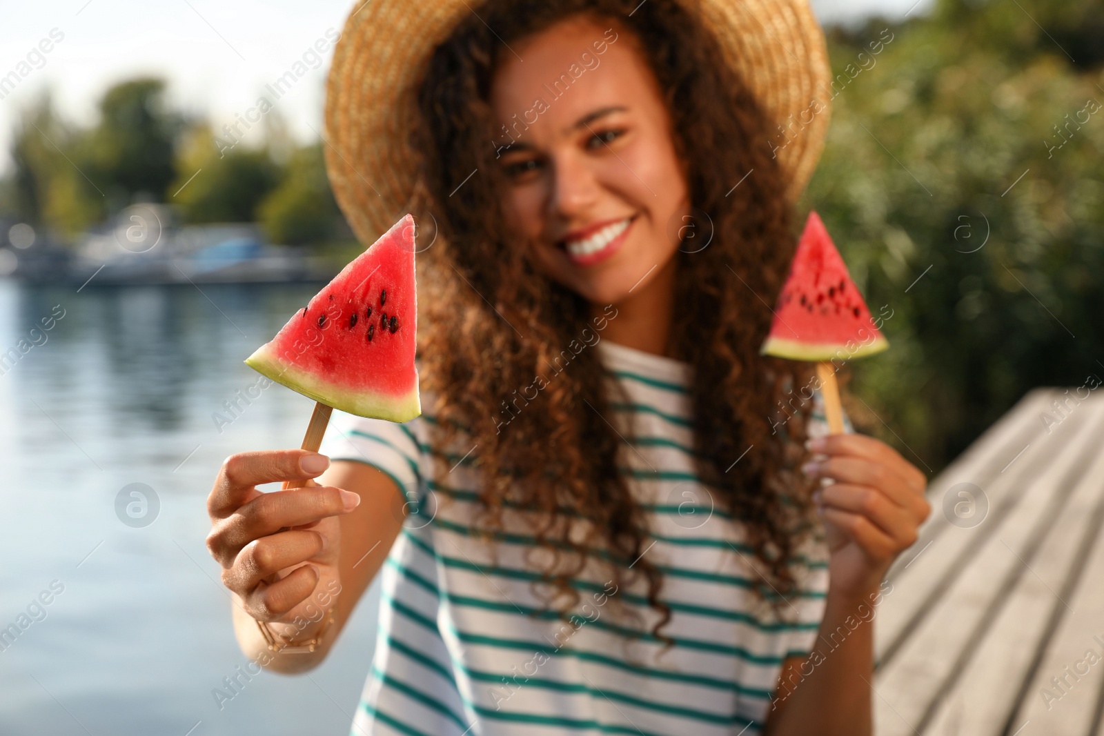 Photo of Beautiful young African American woman with pieces of watermelon near river, focus on hand