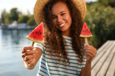Photo of Beautiful young African American woman with pieces of watermelon near river, focus on hand