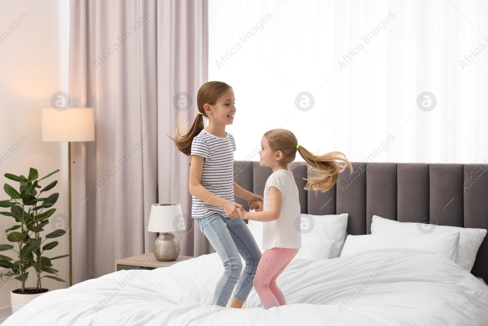 Photo of Cute little sisters having fun together on bed at home