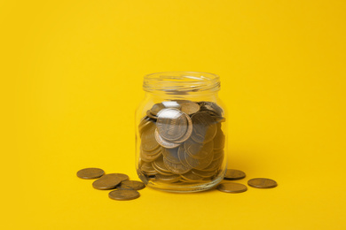 Glass jar with coins on yellow background