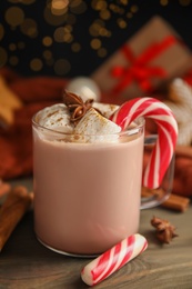 Photo of Glass cup of tasty cocoa with marshmallows and Christmas candy cane on wooden table