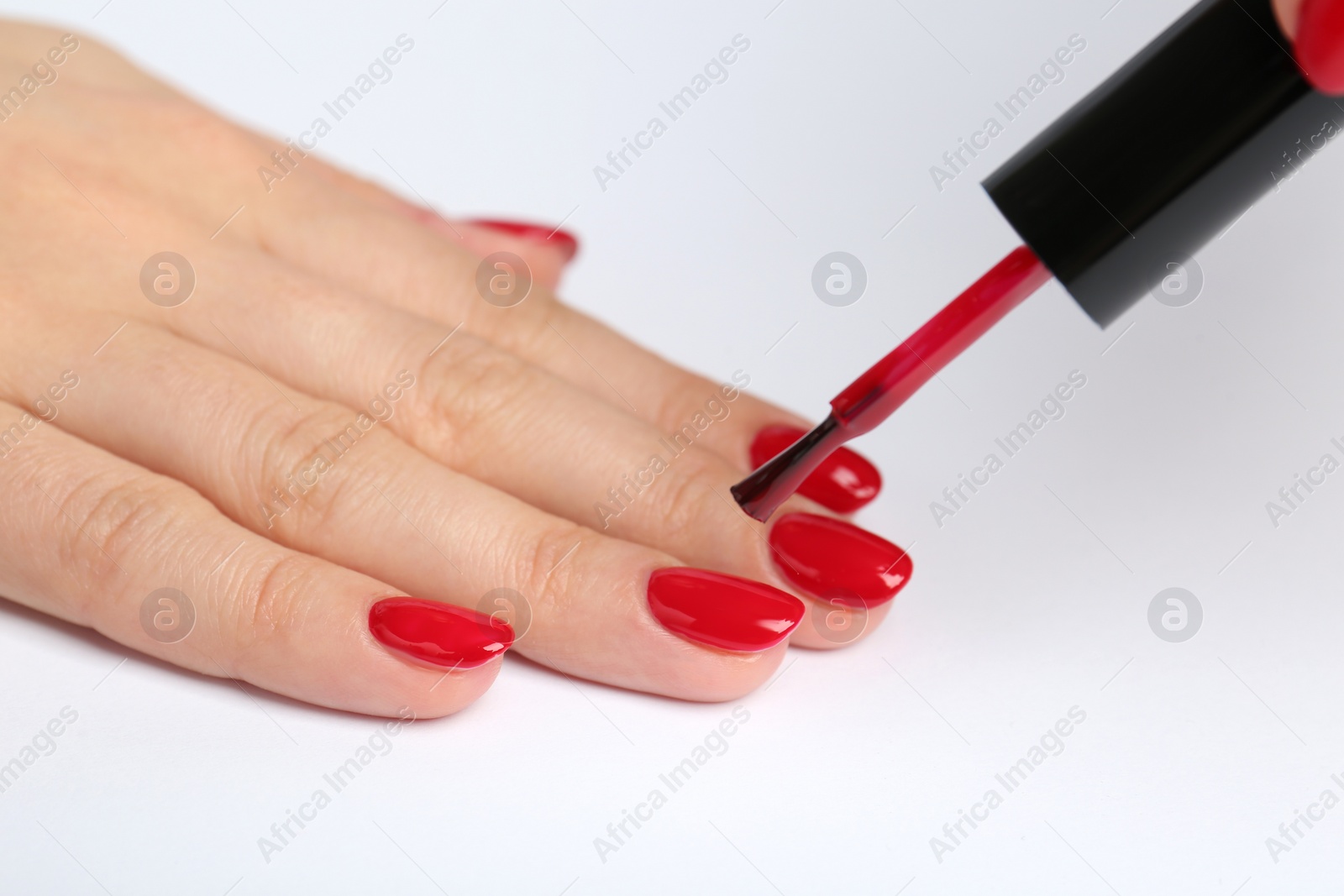 Photo of Woman painting nails with red polish on white background, closeup