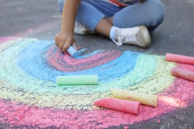 Photo of Little child drawing rainbow with colorful chalk on asphalt, closeup