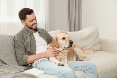 Photo of Happy man sitting on sofa with his cute Labrador Retriever at home