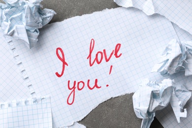 Photo of Note with words I LOVE YOU and crumpled paper on grey table, flat lay