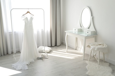 Beautiful wedding dress hanging on clothing rack in room