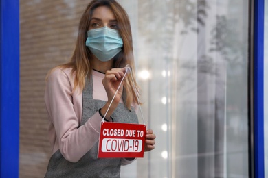 Photo of Business owner in mask hanging red sign with text Closed Due To Covid-19 onto glass door. Coronavirus quarantine