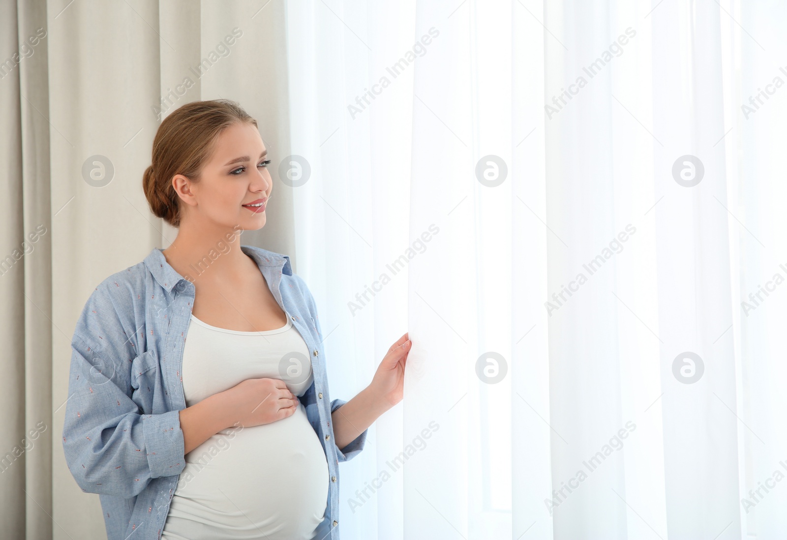 Photo of Young pregnant woman near window at home. Space for text