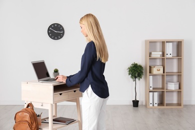 Young woman using laptop at stand up workplace indoors