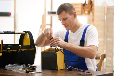 Professional technician repairing electric fan heater with screwdriver at table indoors