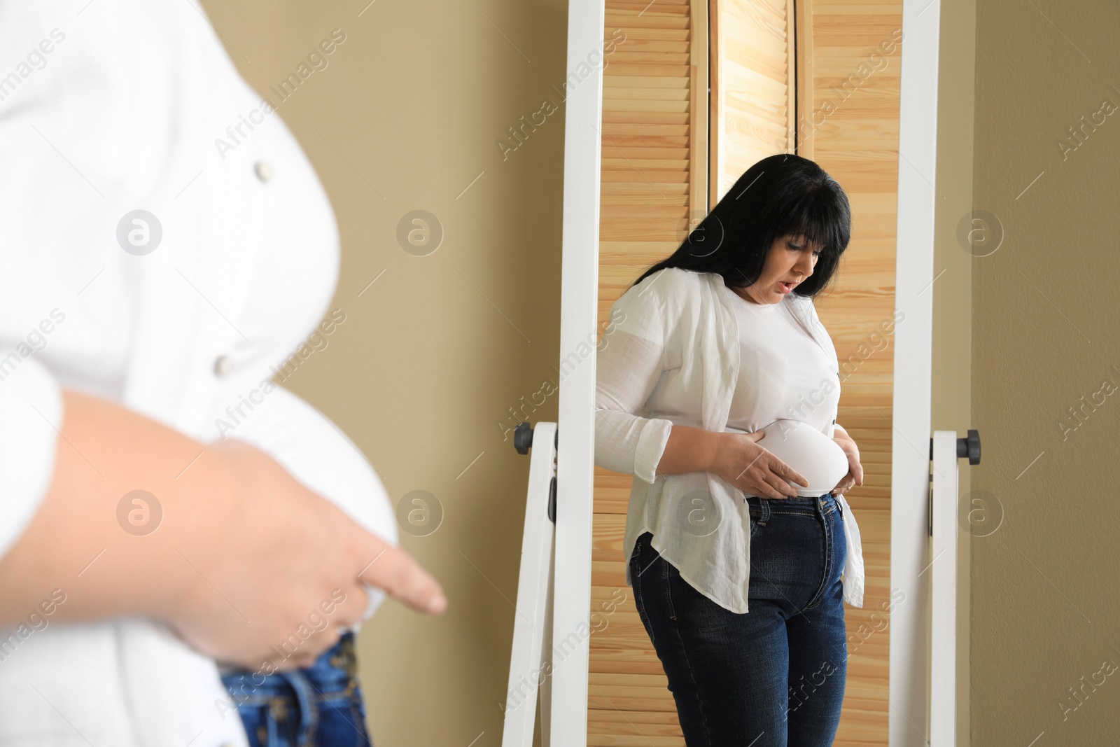 Photo of Overweight woman in tight shirt near mirror at home