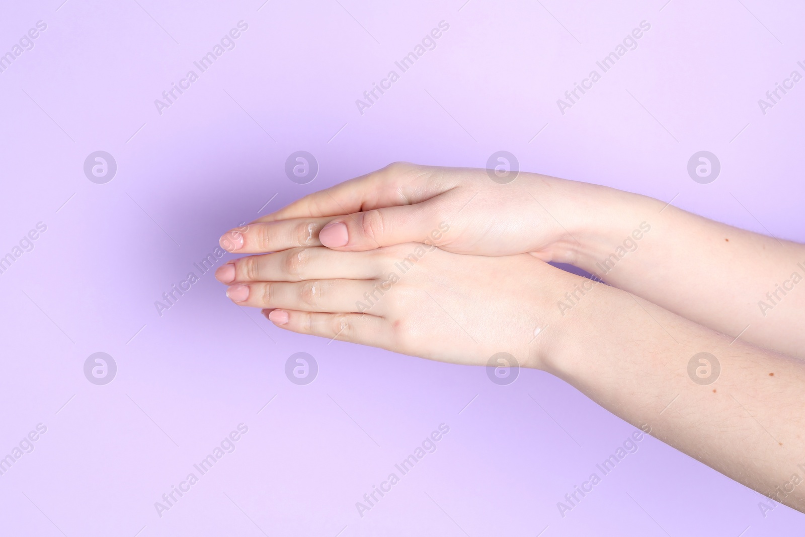 Photo of Woman applying cream on her hand against violet background, closeup