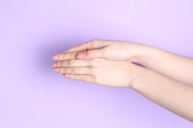 Photo of Woman applying cream on her hand against violet background, closeup