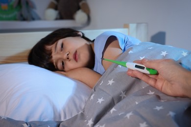 Photo of Doctor with thermometer near sick little boy in bed indoors