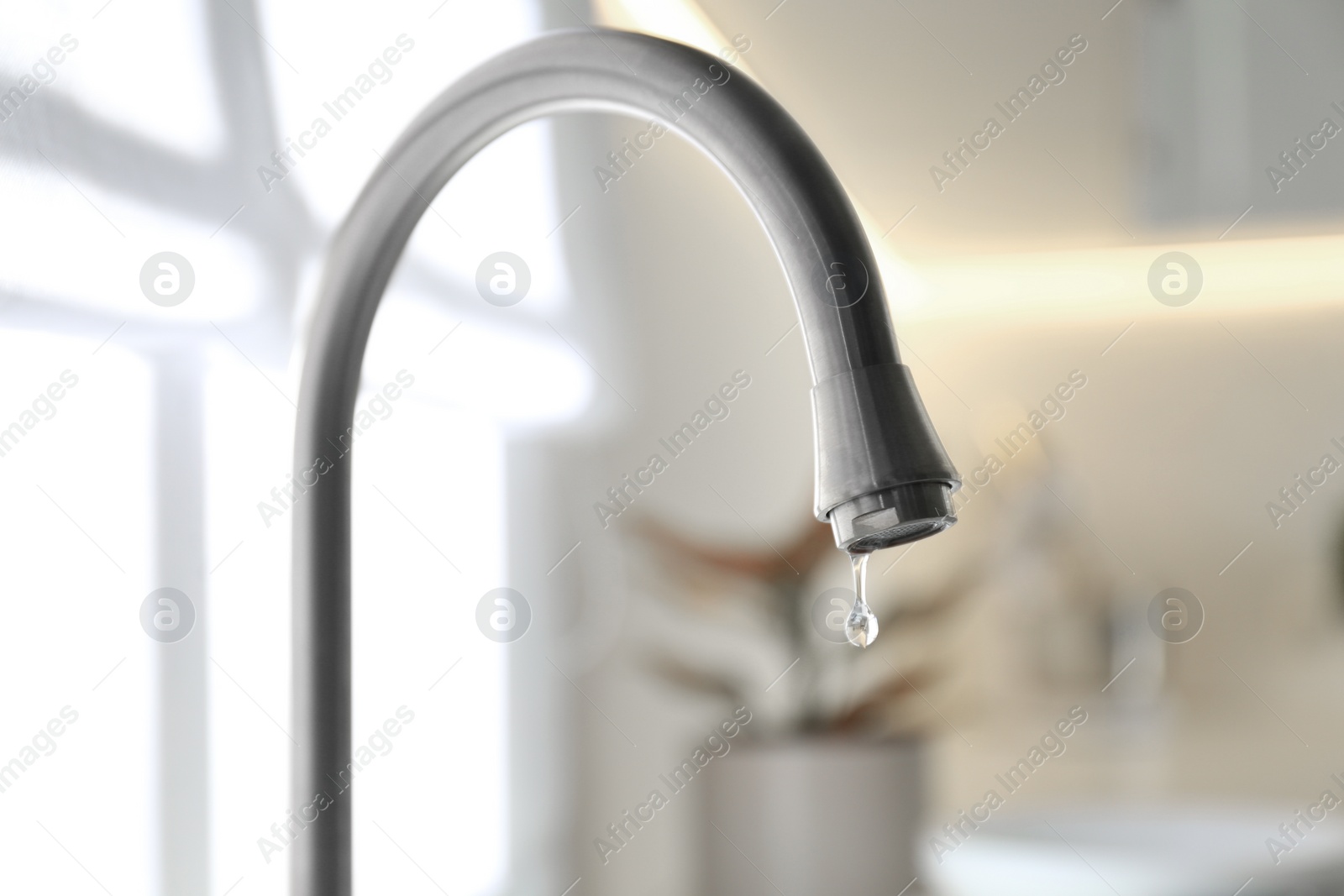 Photo of Water drop falling down from tap on blurred background, closeup