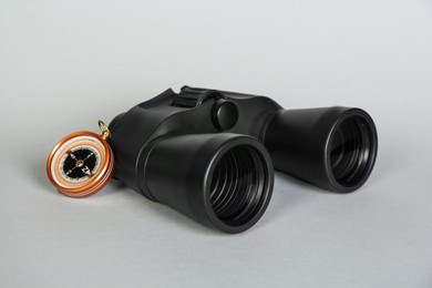 Photo of Modern binoculars and compass on grey background