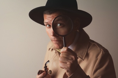 Male detective with smoking pipe looking through magnifying glass on beige background