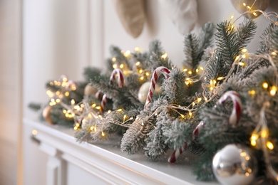 Photo of Beautiful decoration of fir tree branches, candy canes, fairy lights and Christmas balls in room, closeup