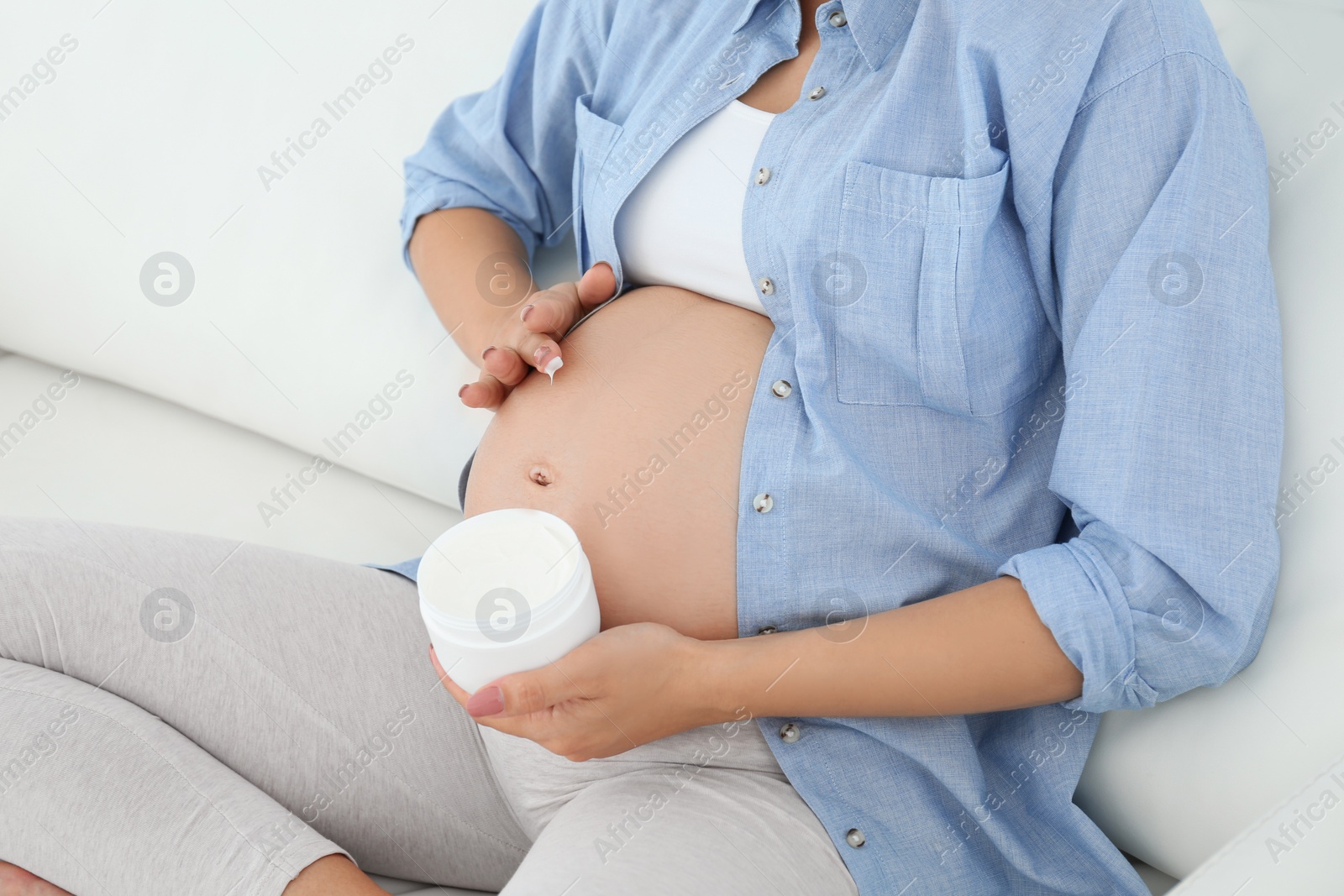 Photo of Pregnant woman applying body cream on belly at home, closeup