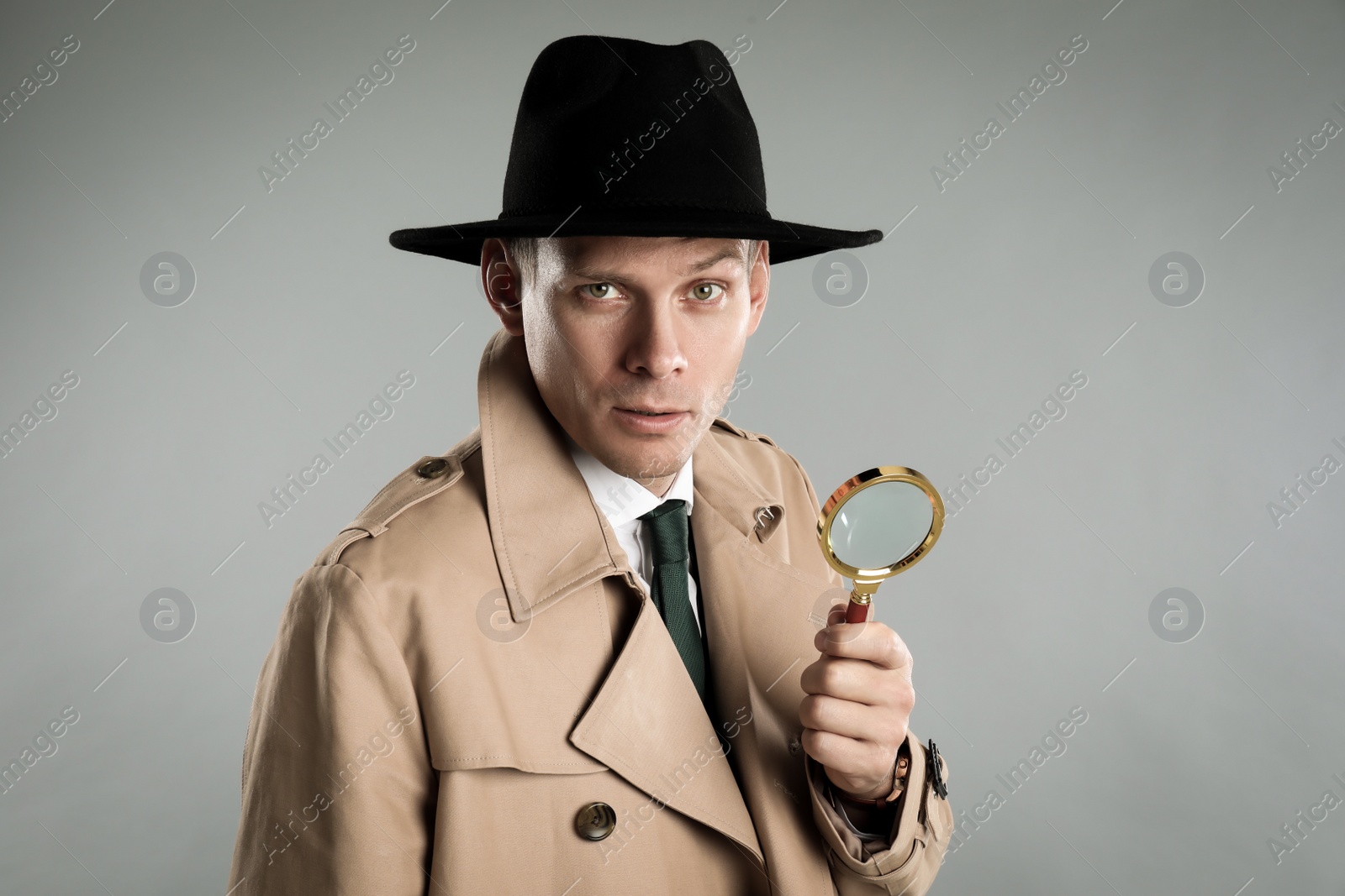 Photo of Male detective with magnifying glass on grey background