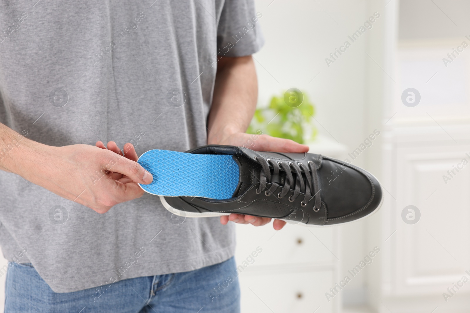 Photo of Man putting orthopedic insole into shoe indoors, closeup