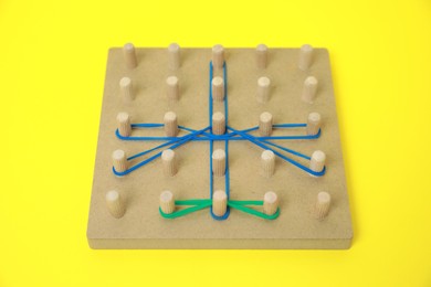 Photo of Wooden geoboard with dragonfly shape made of rubber bands on yellow background. Educational toy for motor skills development