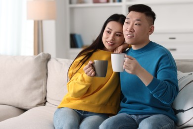 Photo of Happy couple with cups of drink on sofa at home