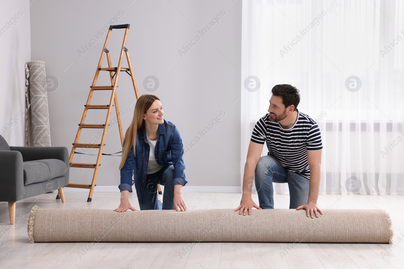 Photo of Smiling couple unrolling new carpet in room