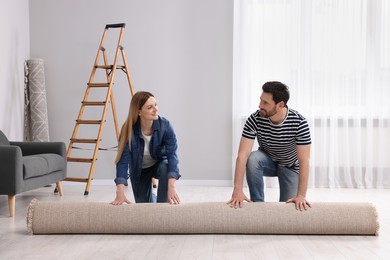 Smiling couple unrolling new carpet in room