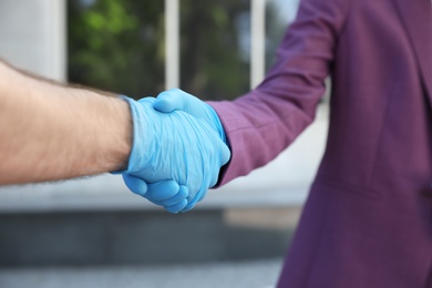 Man and woman in protective gloves shaking hands to say hello outdoors, closeup