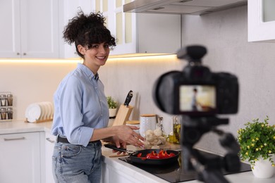 Photo of Smiling food blogger cooking while recording video in kitchen